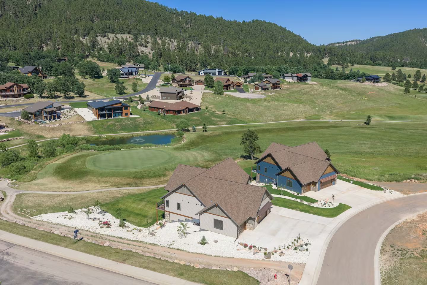 Aerial view of both homes side by side on the golf course at Boulder Canyon, with a green, a pond and the Black Hills behind