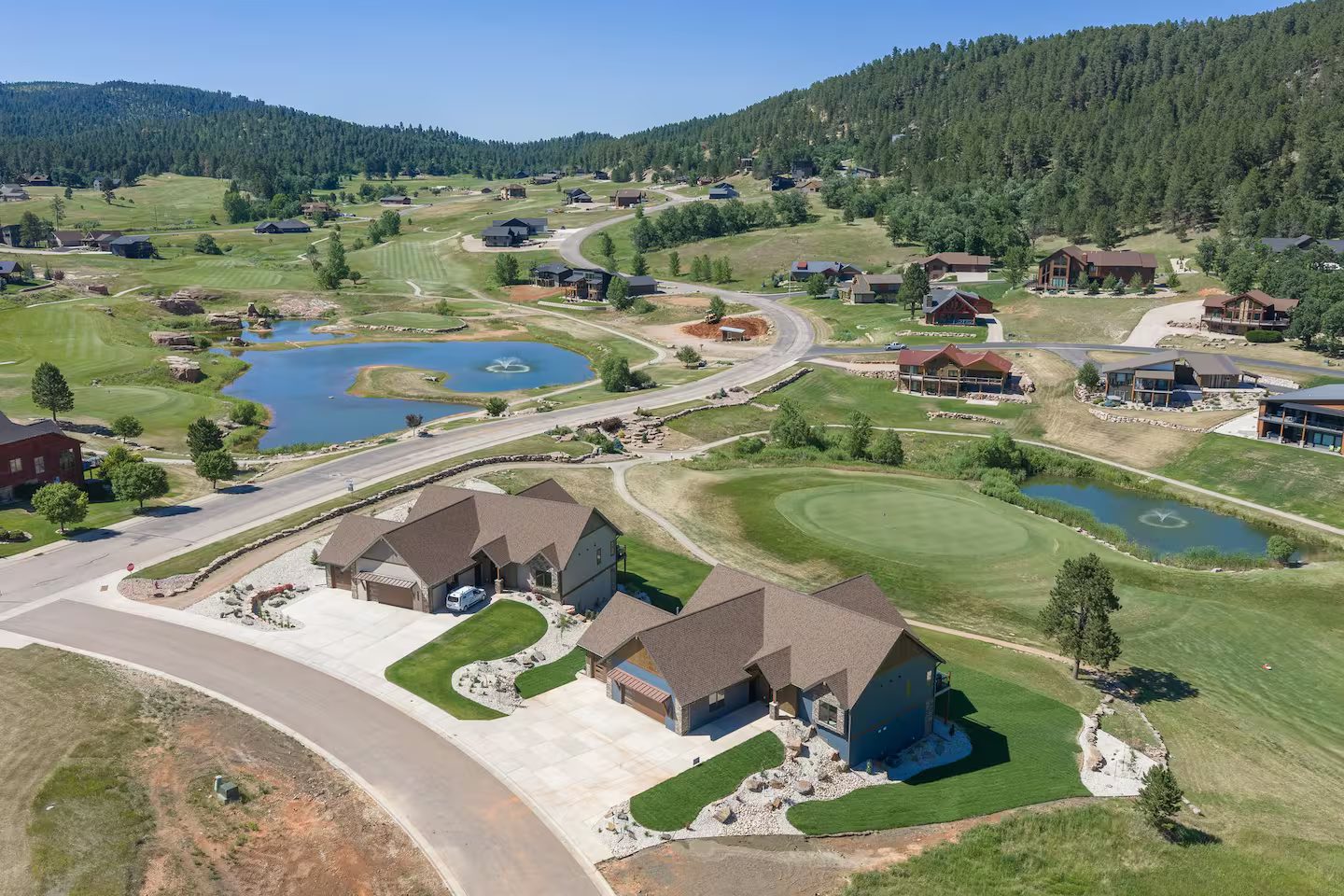 Aerial view of both homes side by side beside a green and pond, with the golf course winding up the valley and the Black Hills on both sides
