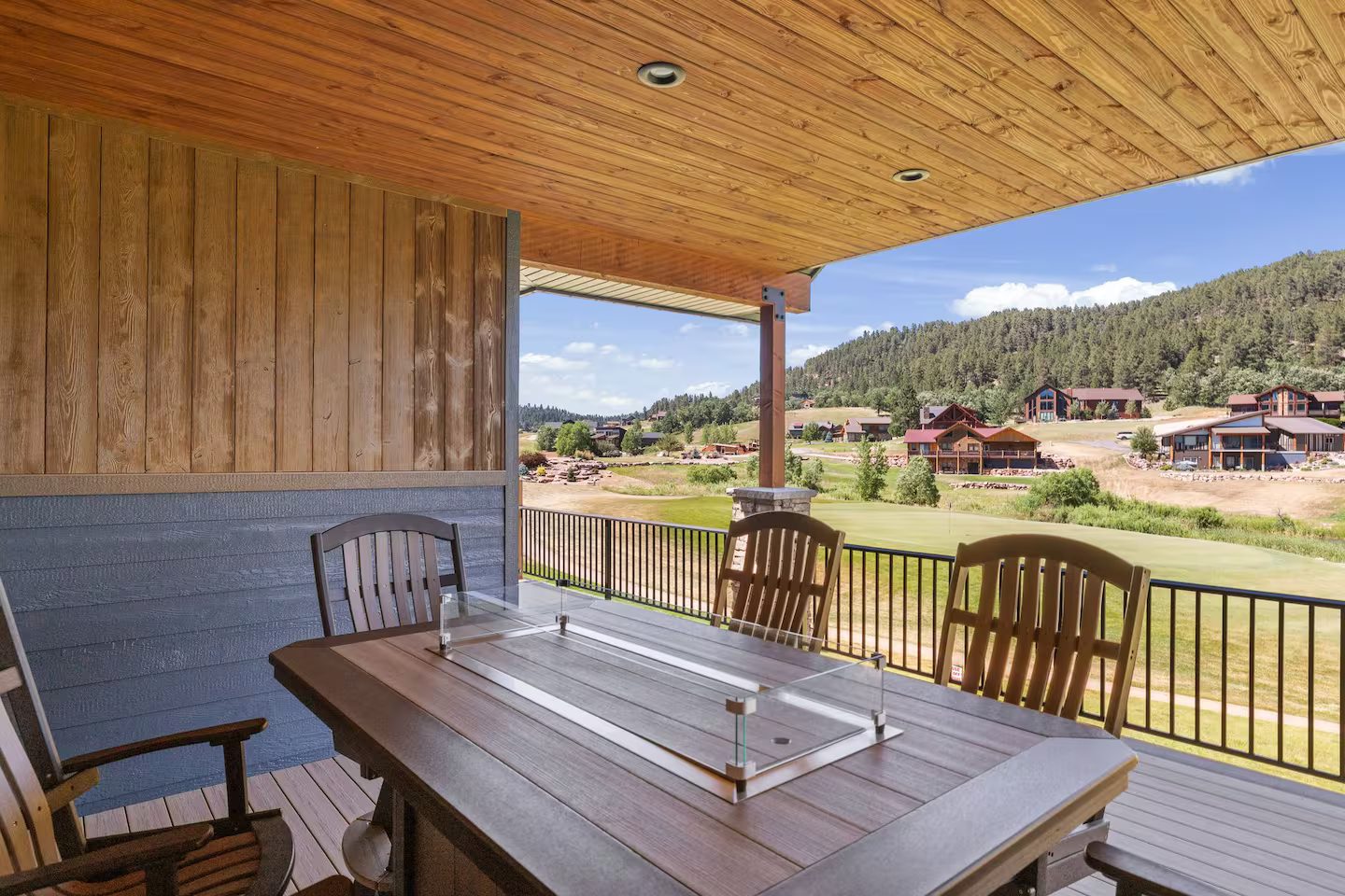 Covered deck at the Luxury Golf Course Retreat with a fire table and chairs, looking out over Boulder Canyon Golf Club and the forested hills