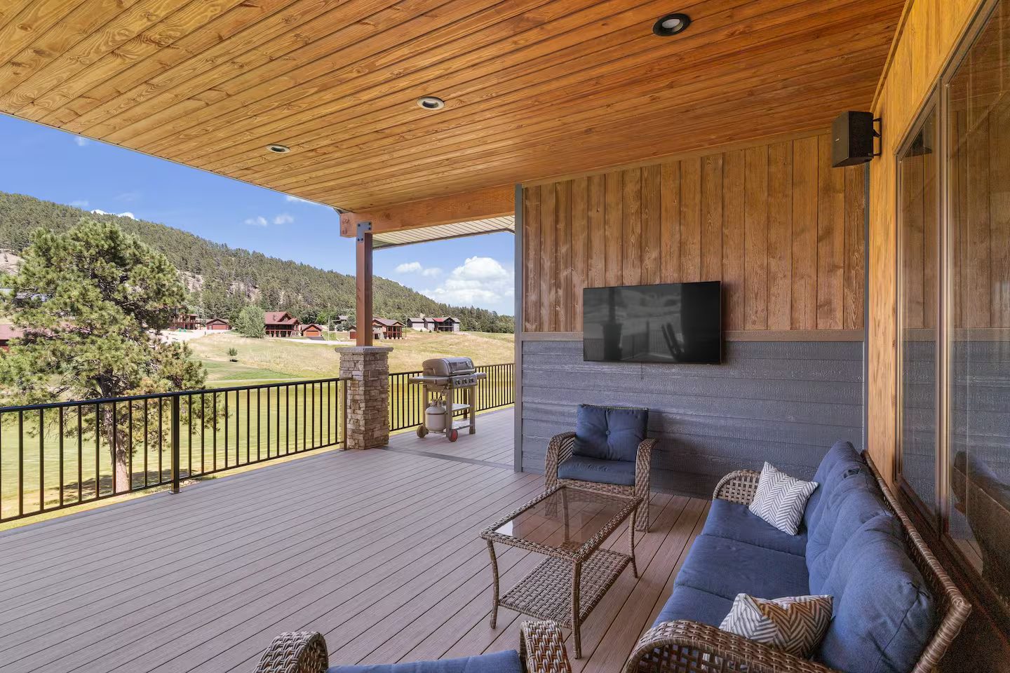 Covered deck with a navy wicker lounge set and an outdoor TV, overlooking the course