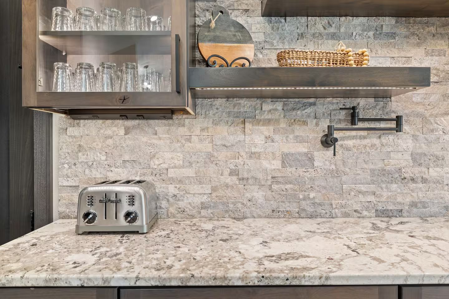 Stacked-stone backsplash with a pot filler and a wood floating shelf