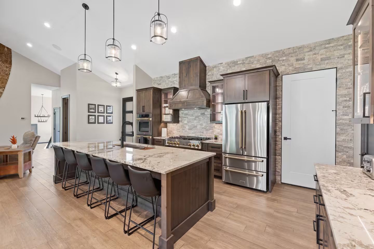 Kitchen with a long stone island and barstools, a wood hood and a French-door refrigerator
