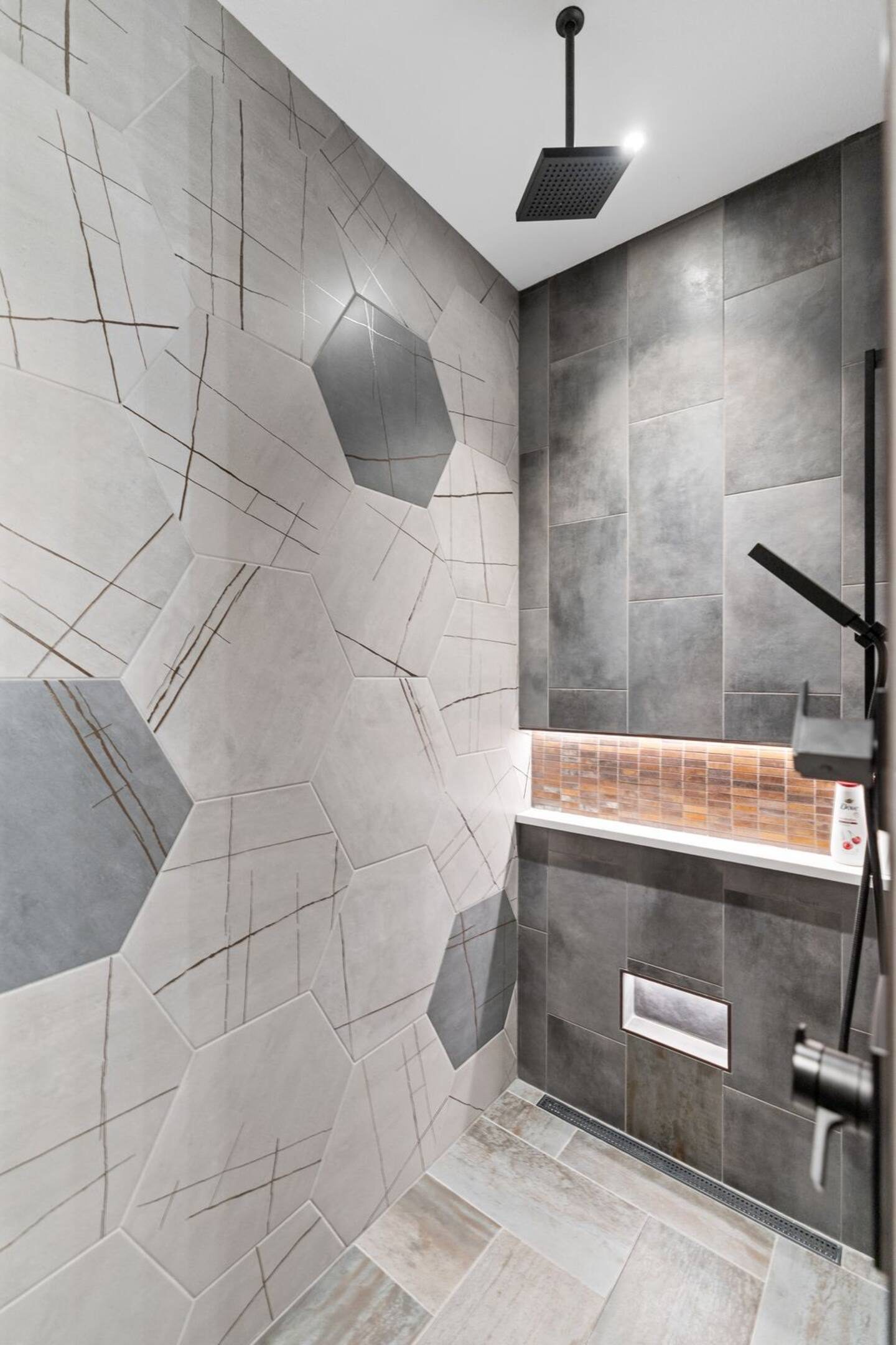 Walk-in shower at the Luxury Golf Course Retreat with oversized hexagon tile, a lit niche with a copper mosaic, and a matte black rain head and handheld sprayer
