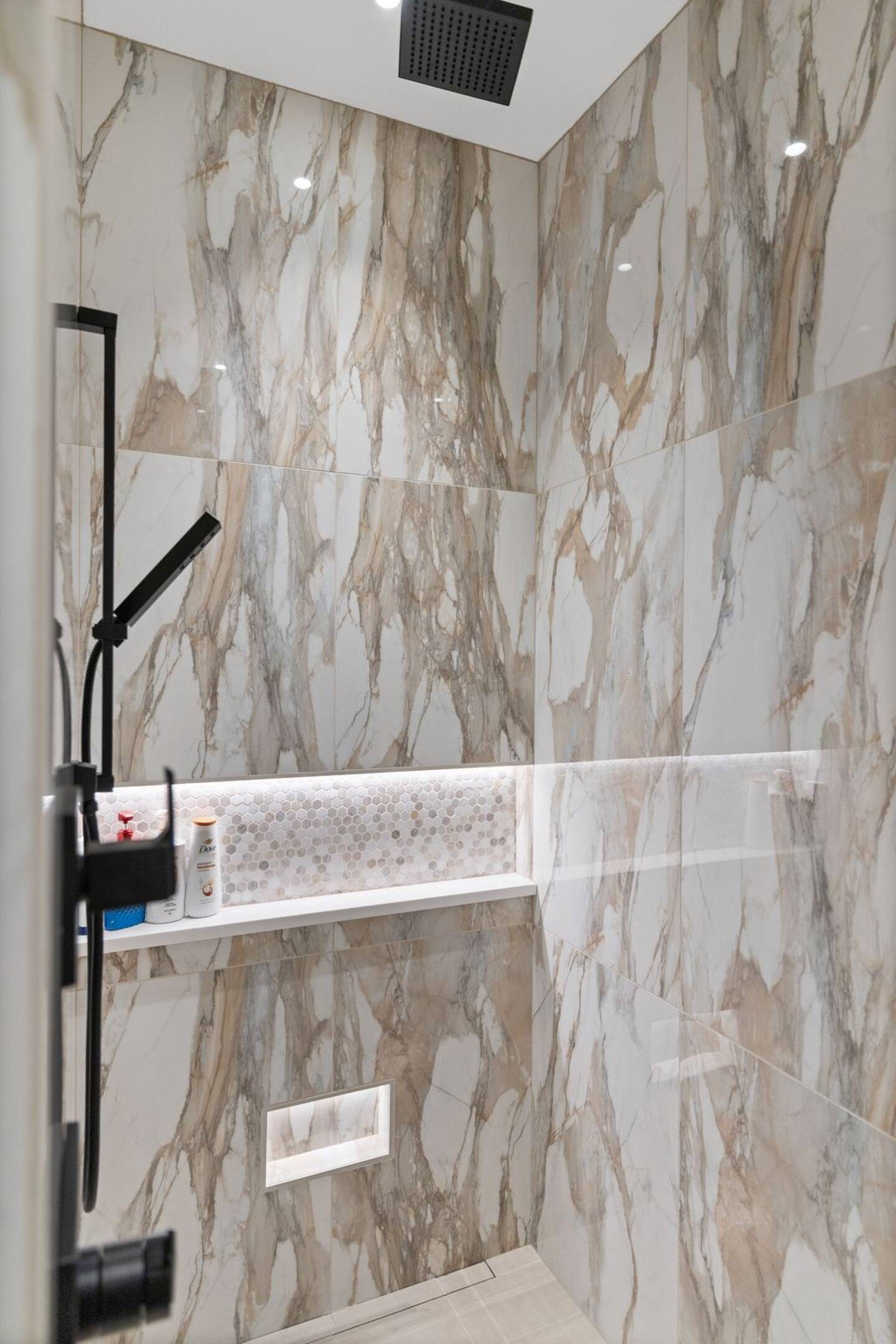 Walk-in shower in marble-look slab with a lit niche and black fixtures