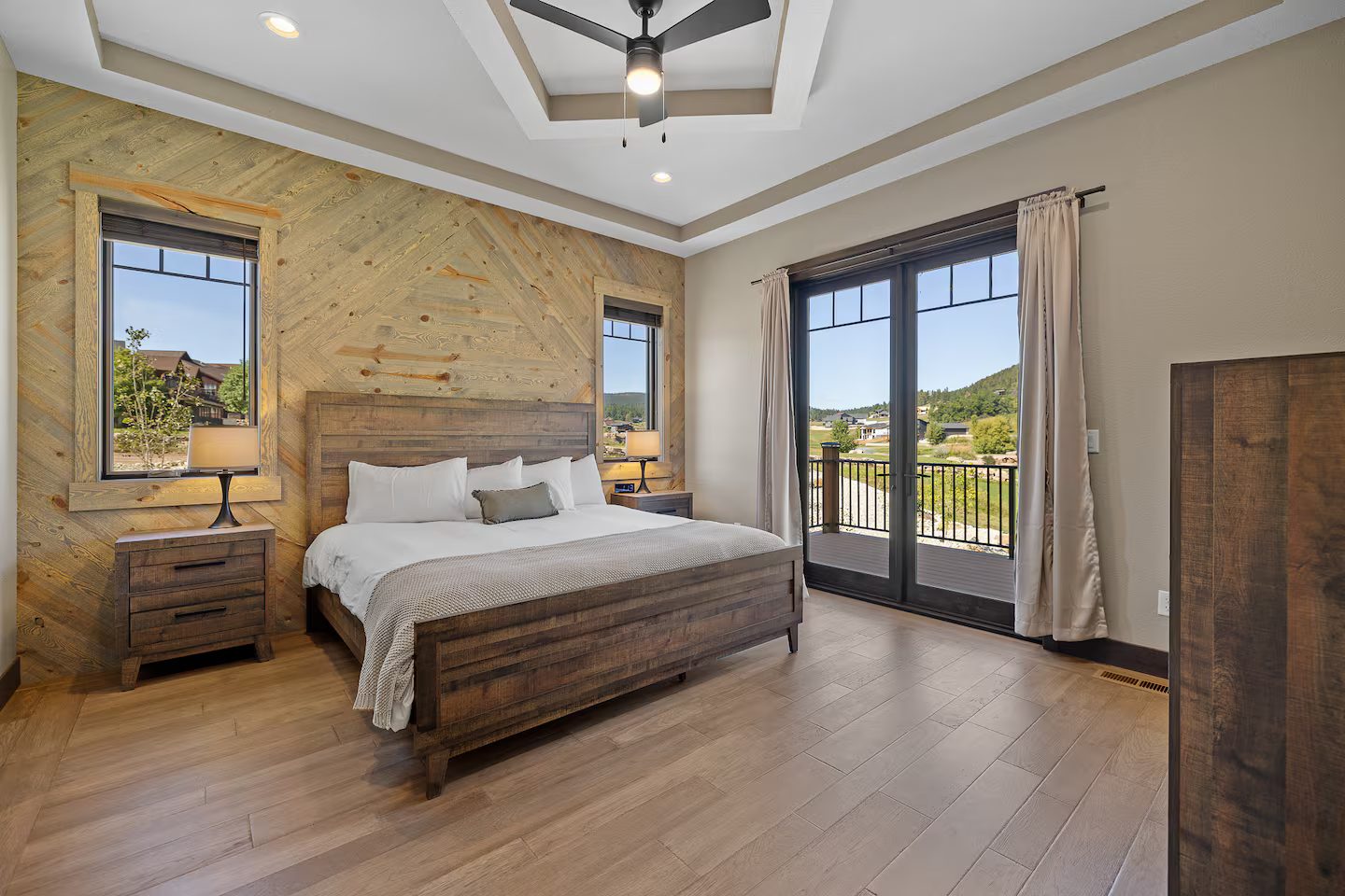 King bedroom with a herringbone wood accent wall, a tray ceiling with a fan and French doors to a deck