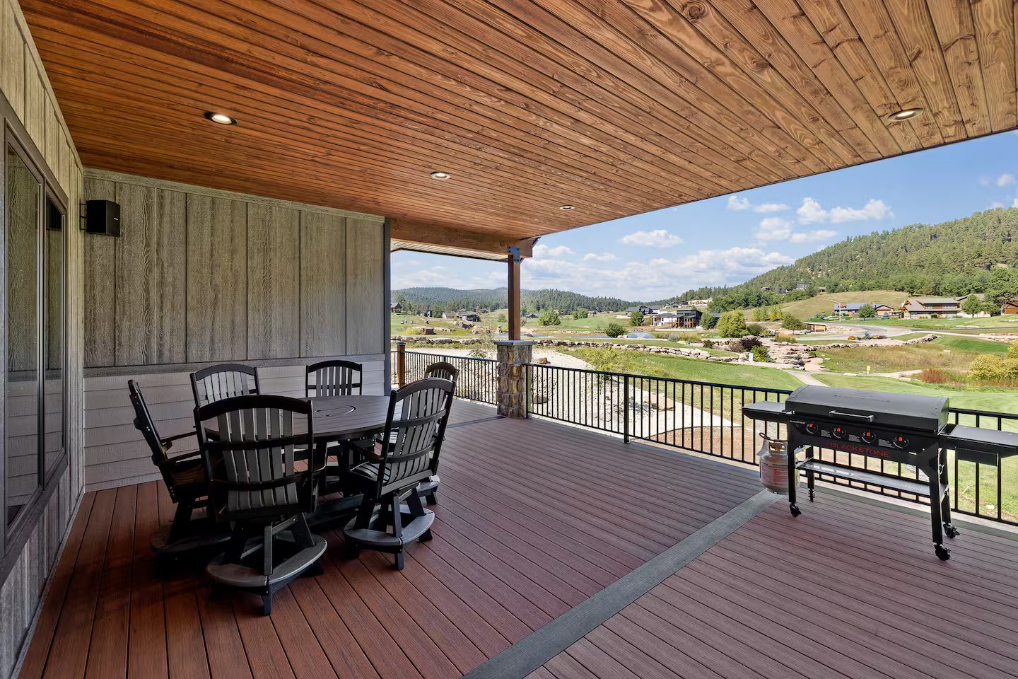Covered deck with a dining table for six and a gas grill, overlooking the course