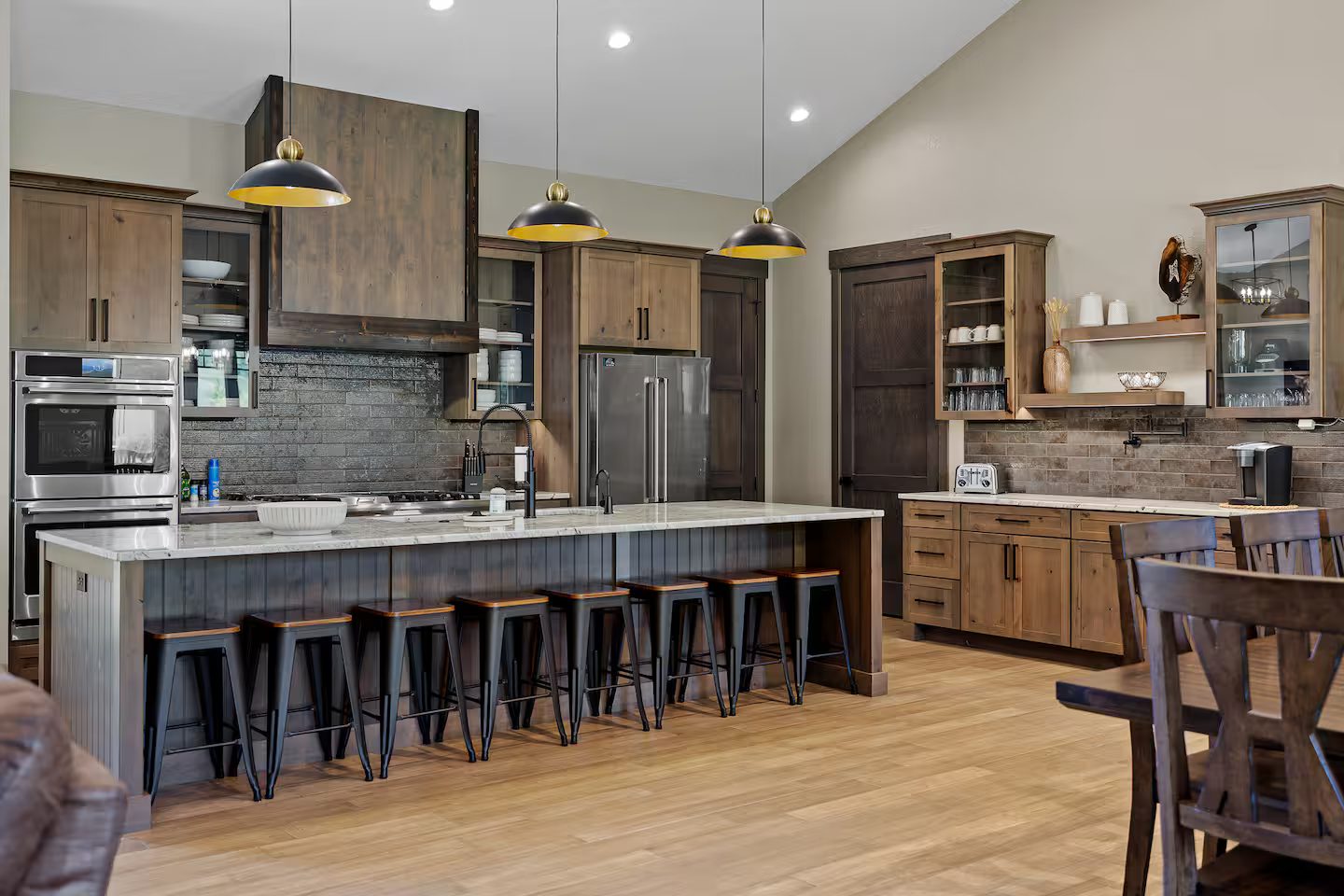 Kitchen with a long island and eight black barstools, wood cabinets, stainless appliances and a coffee bar