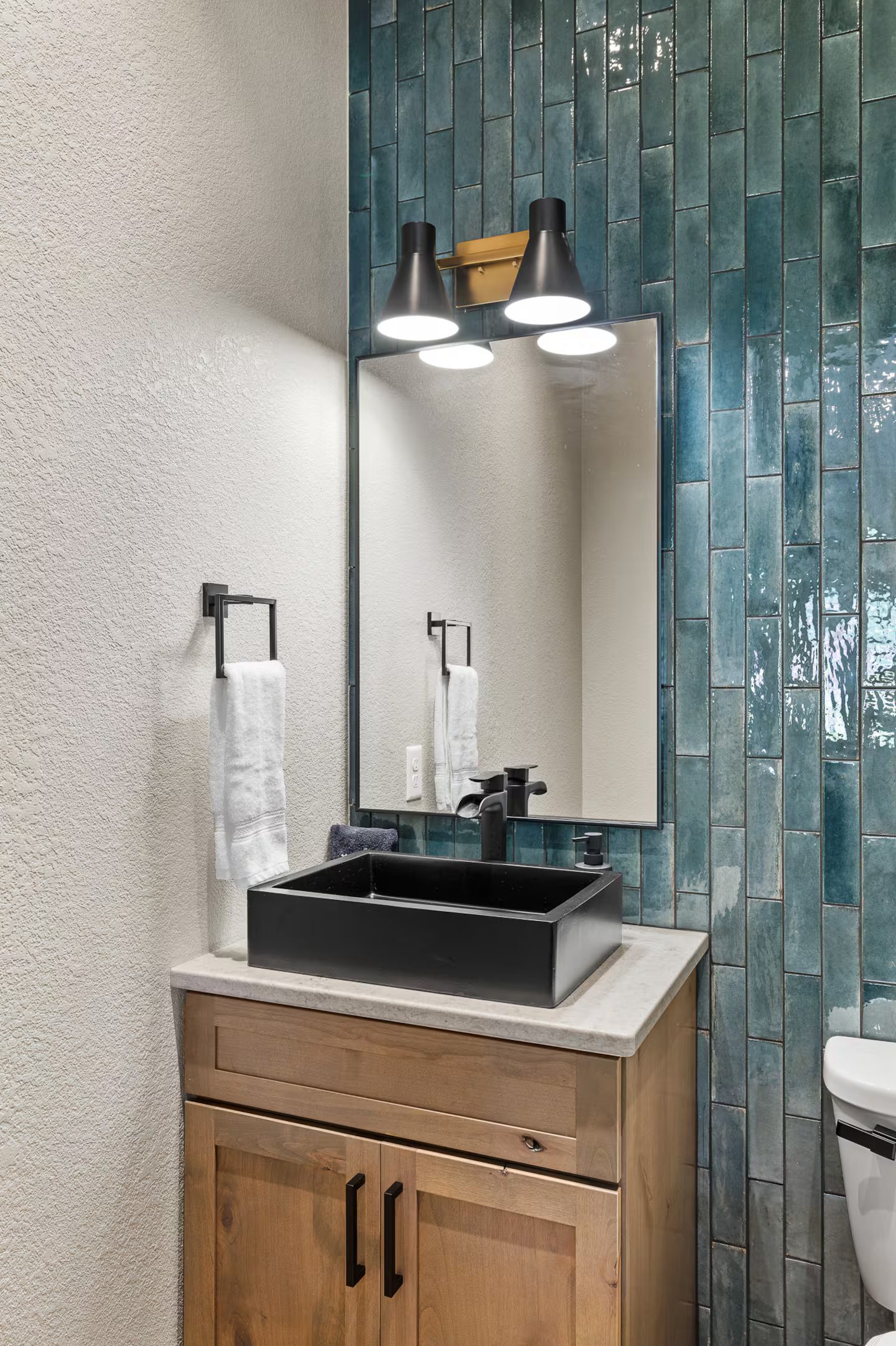 Powder room at the Luxury Black Hills Retreat with glossy teal tile, a black vessel sink and a knotty alder vanity