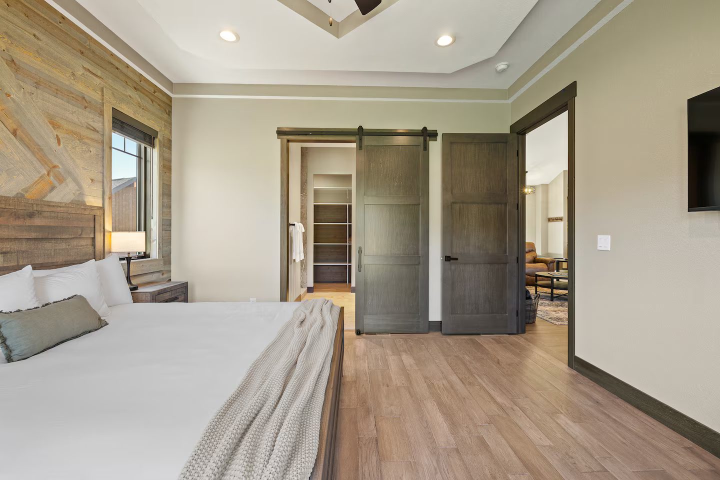 King bedroom with a wood plank accent wall and a sliding barn door to the bath
