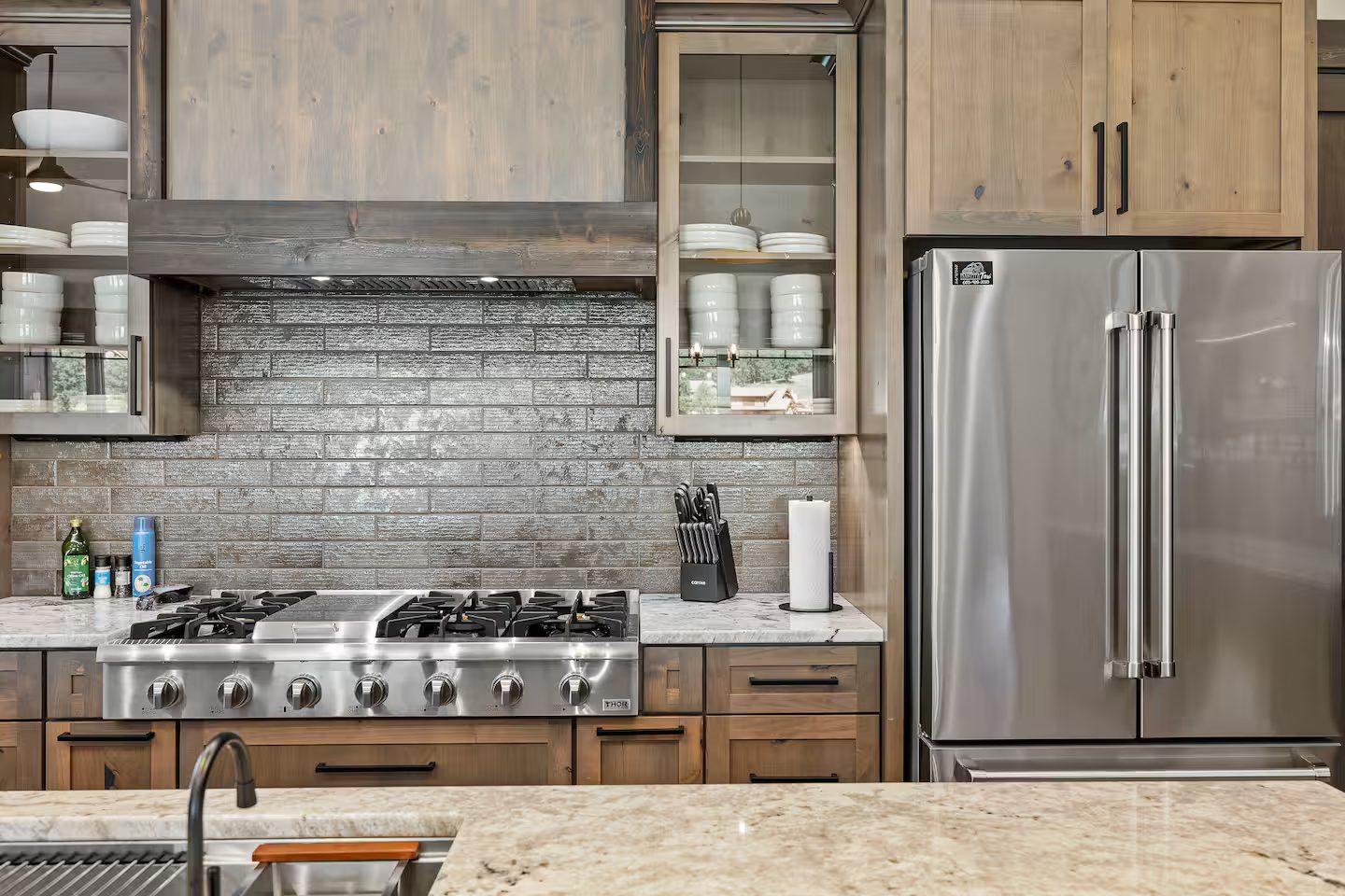 Stainless six-burner range with a griddle under a wood hood, beside a French-door refrigerator