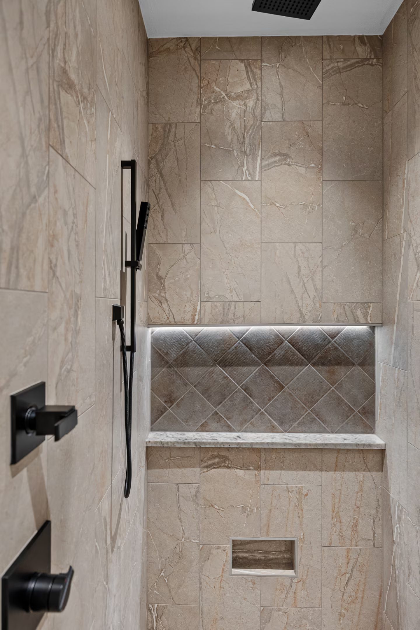 Walk-in tiled shower with a lit niche and a handheld sprayer