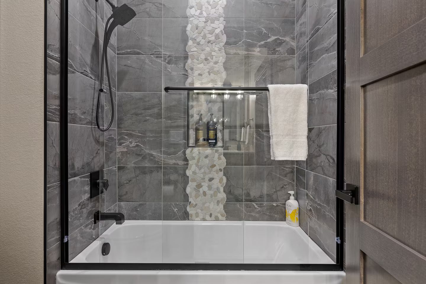 Tiled tub and shower with a glass door and a stone mosaic accent strip